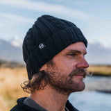 Man wearing a black cable merino wool beanie by Mount Kiwi outdoors near a river with mountains in the background