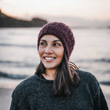 Woman wearing a maroon knit beanie and dark sweater standing outdoors with a blurred natural background